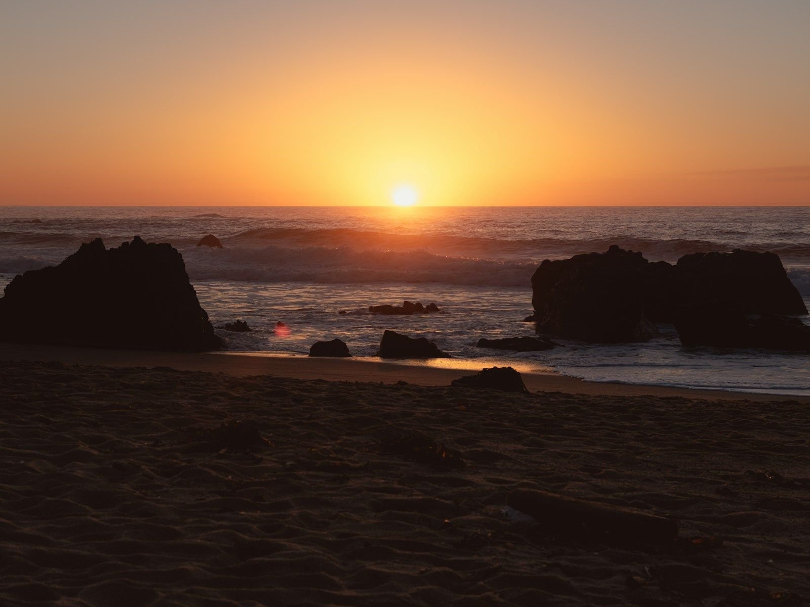 the sun is setting over the ocean on the beach